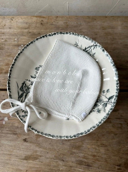 Knitted baby bonnet on a decorative plate with floral patterns