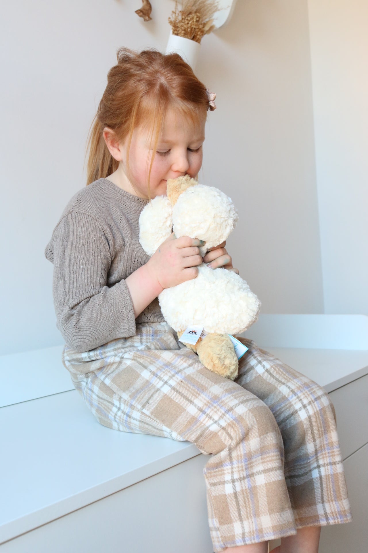 Child playing with a plush toy on a white drawer set.