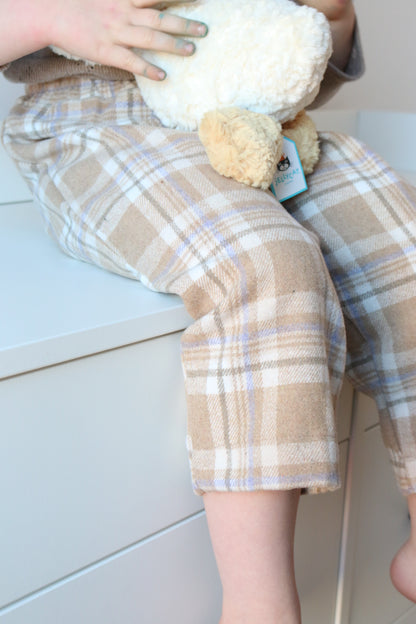 Person wearing plaid pants holding a white duck toy on a light-colored floor.
