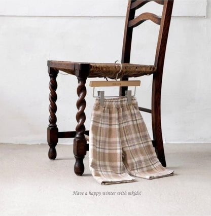 Plaid pants hanging on a wooden chair with a minimal background