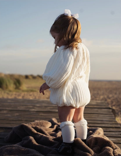 Child in a white outfit standing on a wooden platform with a scenic background