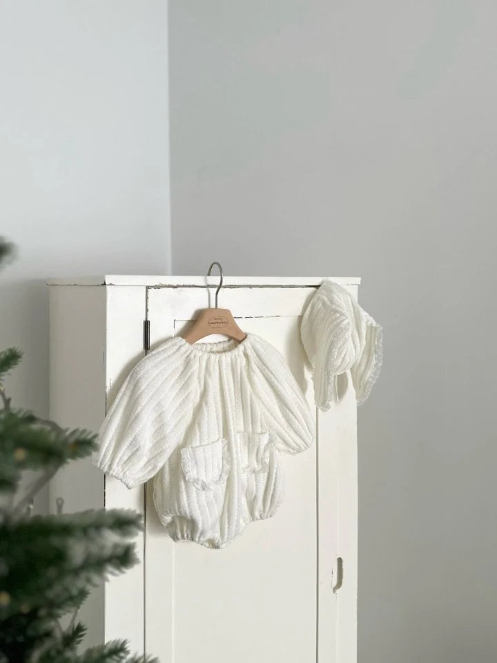 White baby romper on a hanger against a white wall 