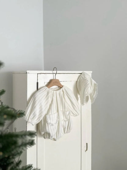 White baby romper on a hanger against a white wall 