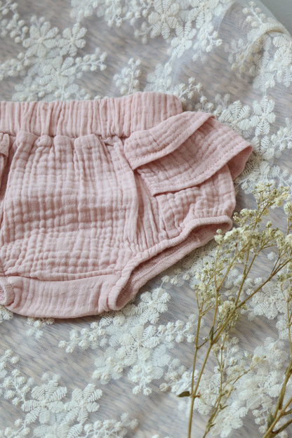 Pink baby bloomers on a textured fabric background with dried flowers