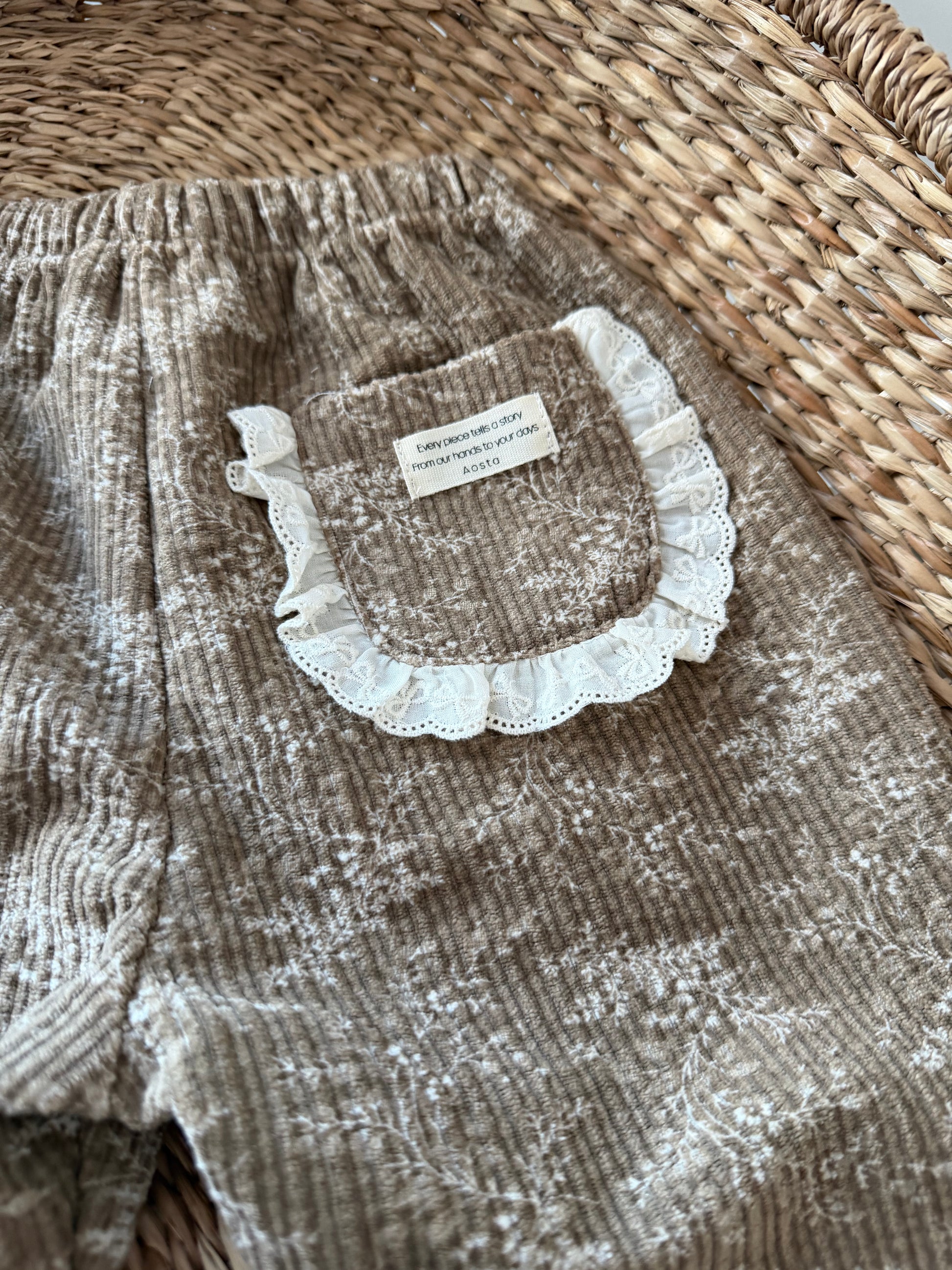 Brown corduroy pants with lace trim on a wicker surface