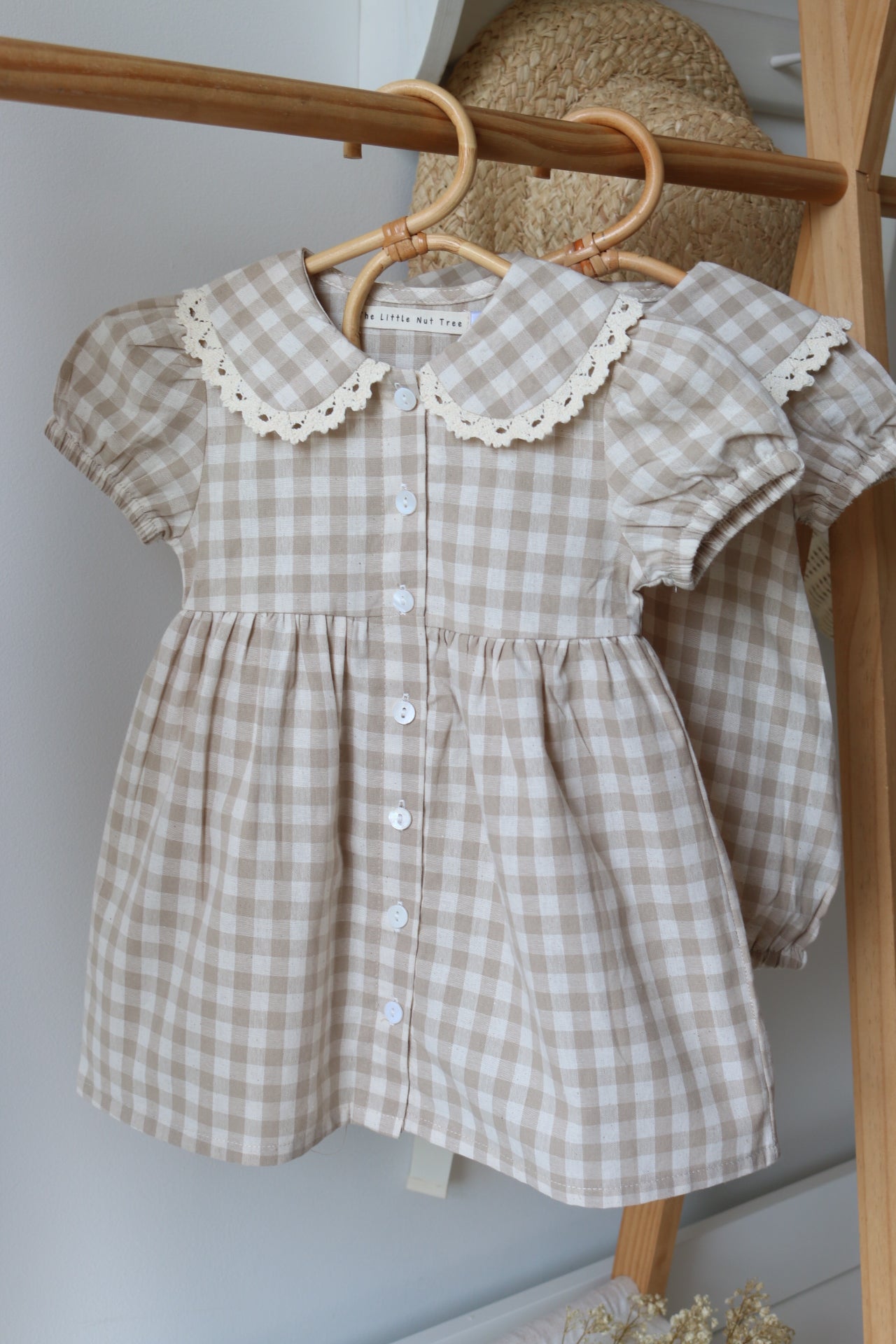 Checkered baby dress with lace details on a wooden rack.