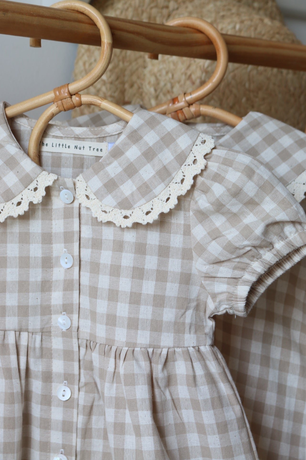Beige checkered baby dress with lace trim on a wooden chair.