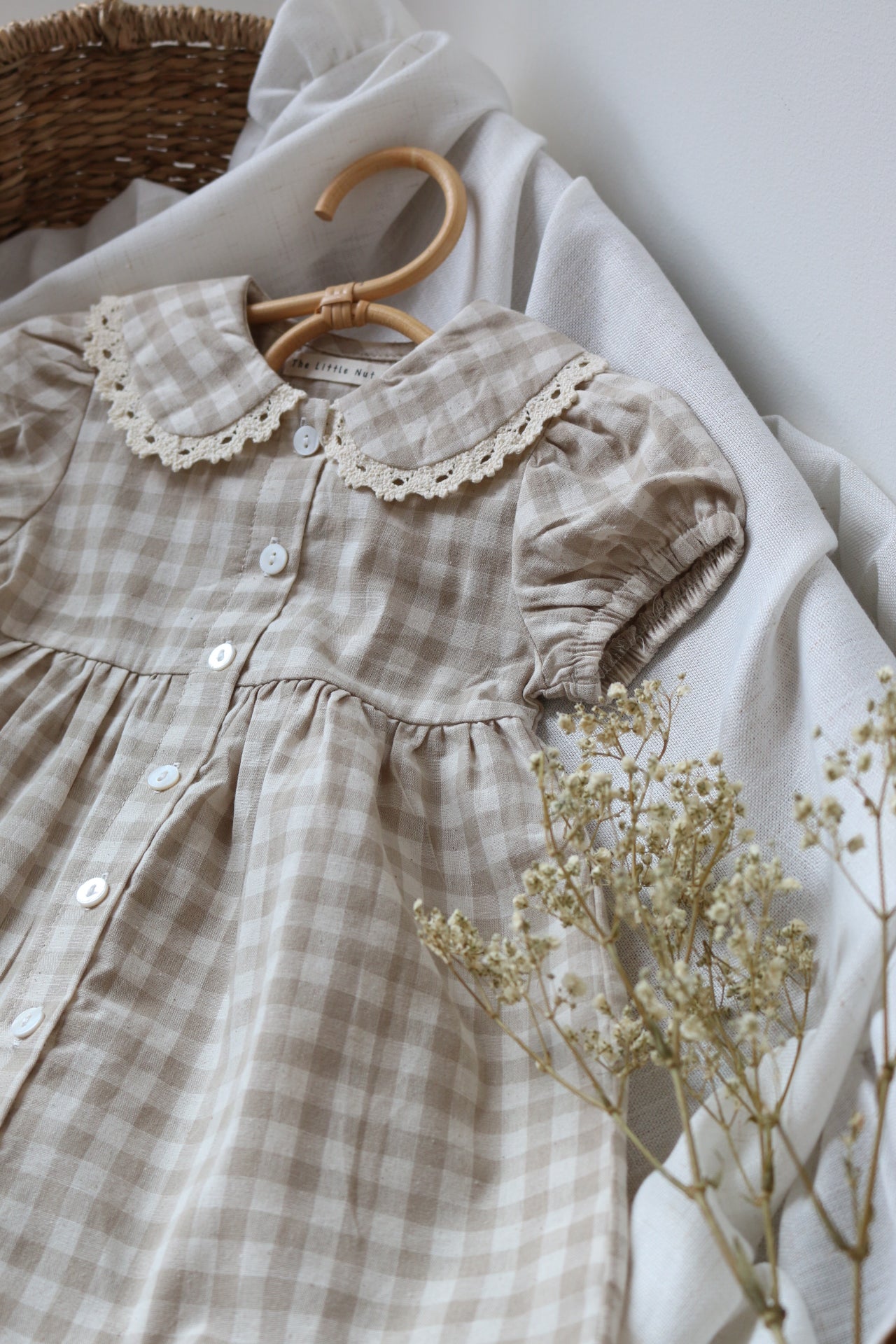 Checkered dress with lace details and dried flowers on a white surface