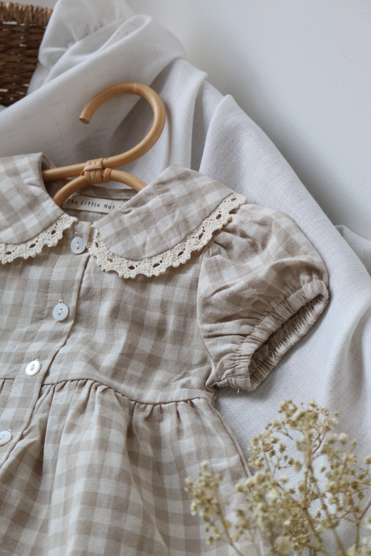 Brown checkered dress with lace details on a white surface with a small plant.