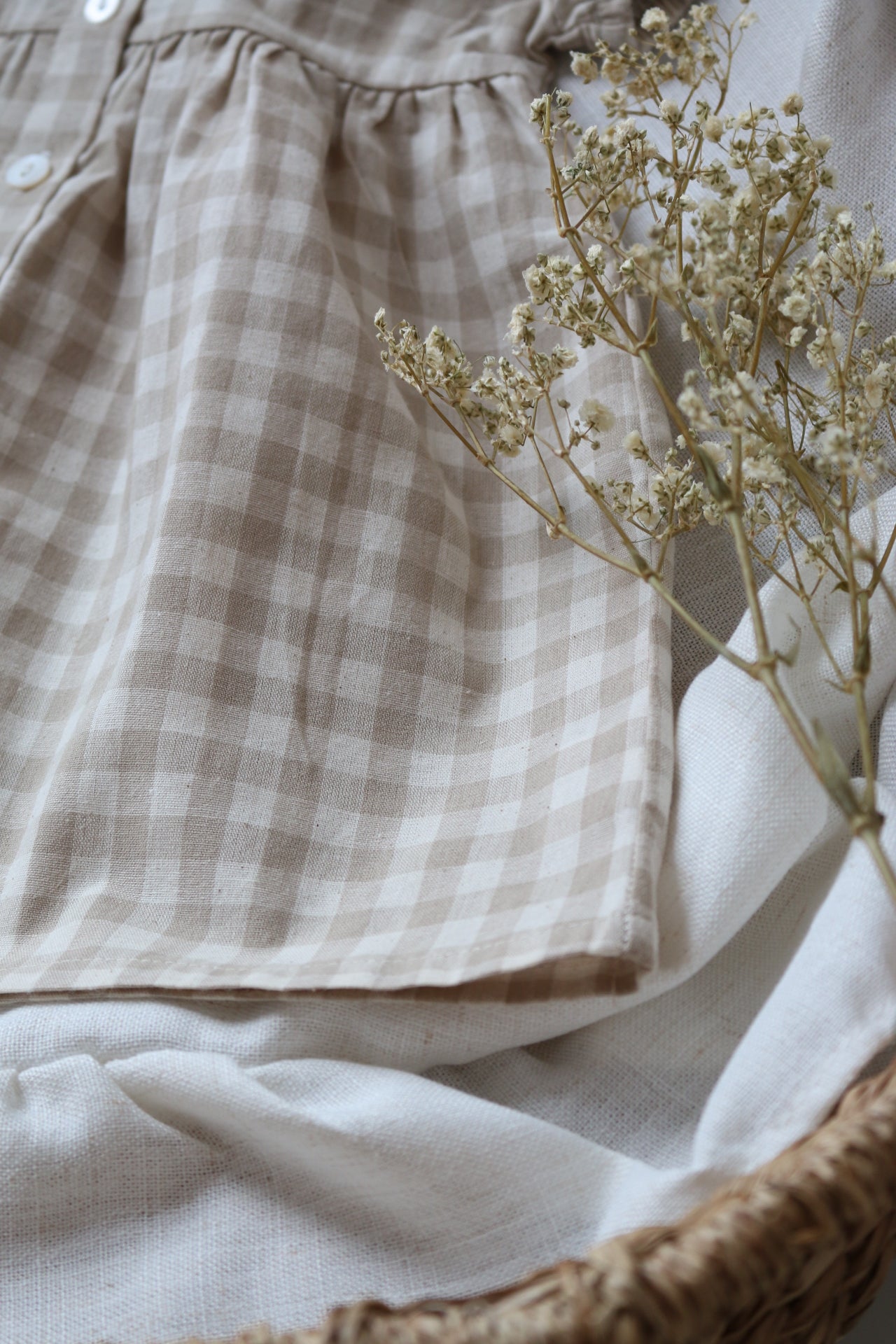 Brown checkered dress with dried flowers on a white surface