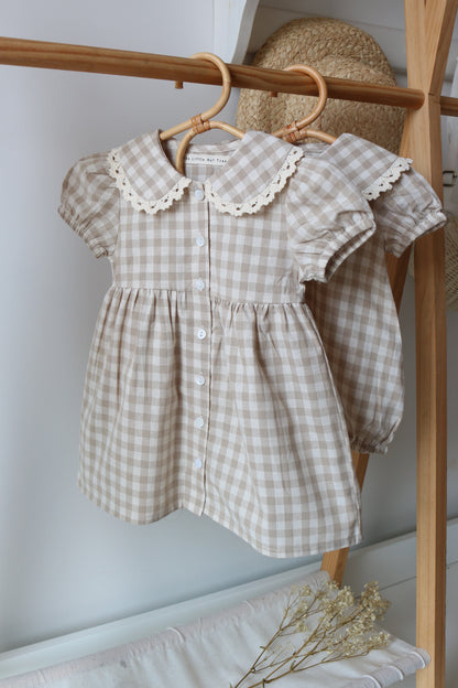 Brown checkered dress with lace details on a wooden hanger against a white wall.