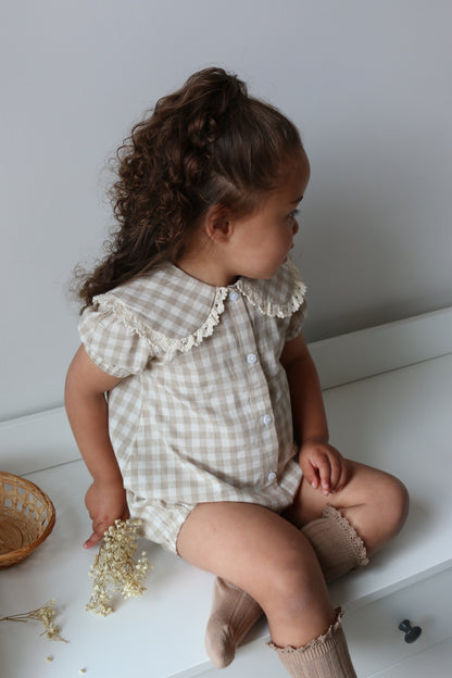 Child in a checkered romper holding dried flowers on a white floor.
