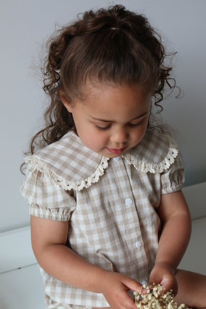 Child wearing a checkered romper holding a small object on a light background