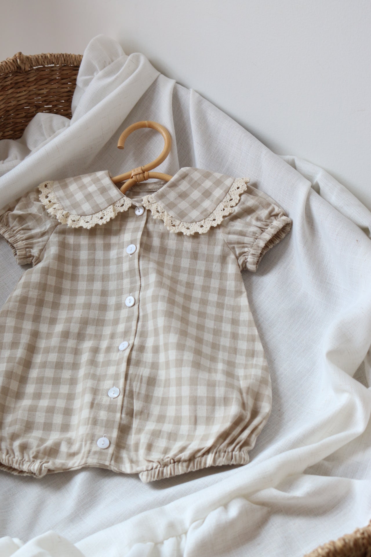 Checkered baby romper with lace collar on a white fabric background