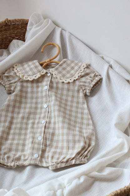 Checkered baby romper with lace collar on a white fabric background
