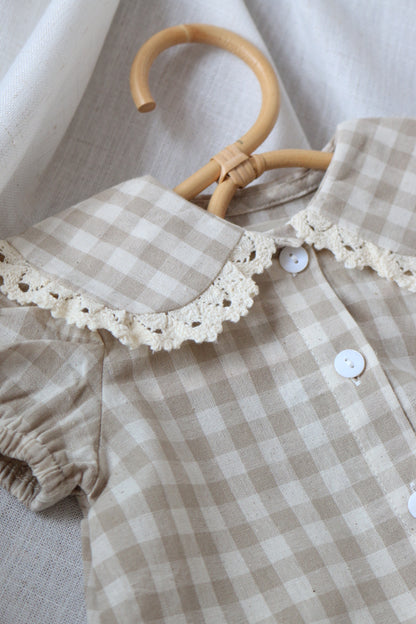 Checkered baby romper with lace collar on a hanger