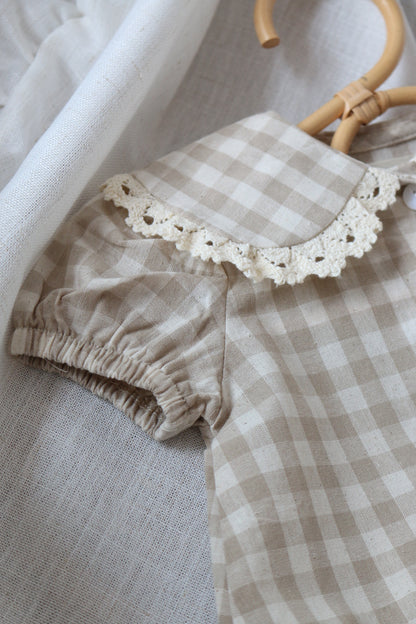Checkered baby outfit with lace collar on a neutral background
