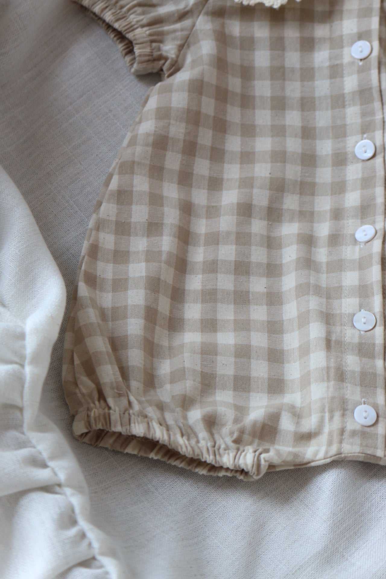 Beige and white checkered baby romper on a light background