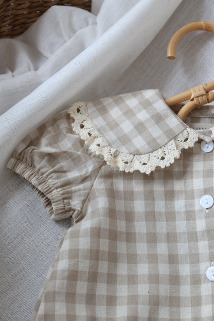 Plaid romper with lace collar on a textured surface