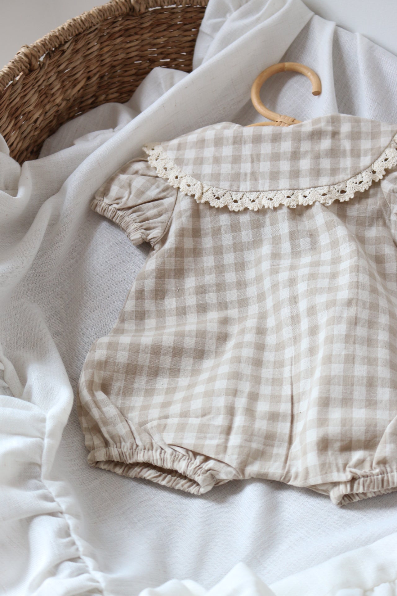 Plaid baby romper with lace trim on a white fabric background
