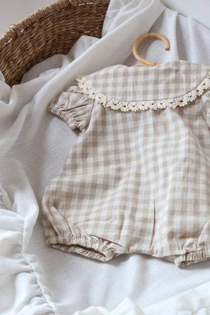 Plaid baby romper with lace trim on a white fabric background