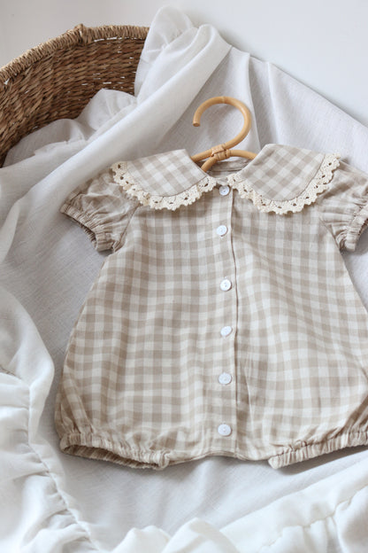 Checkered baby romper with lace trim on a white fabric background