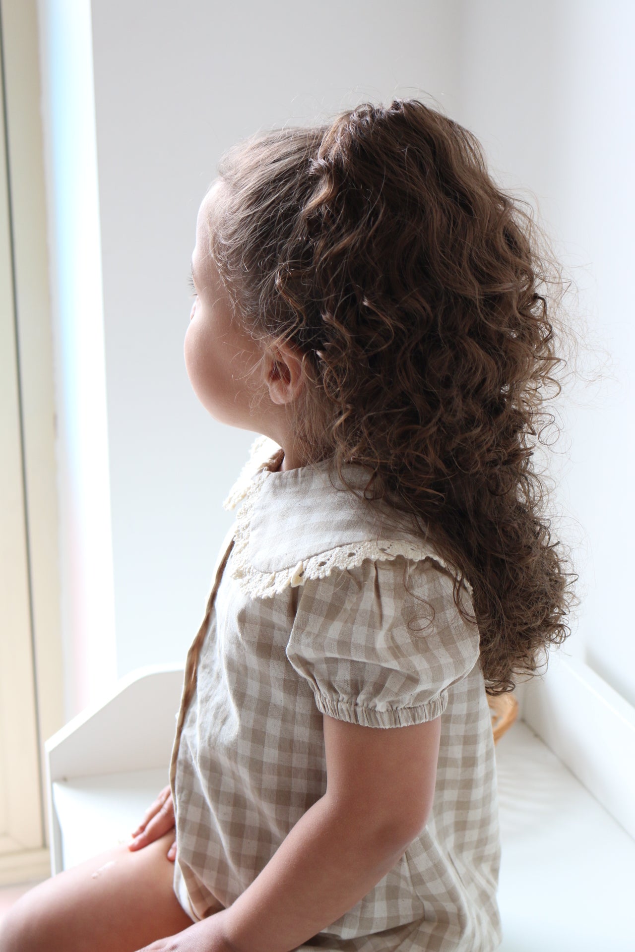 Child wearing a checkered romper standing indoors with a neutral background