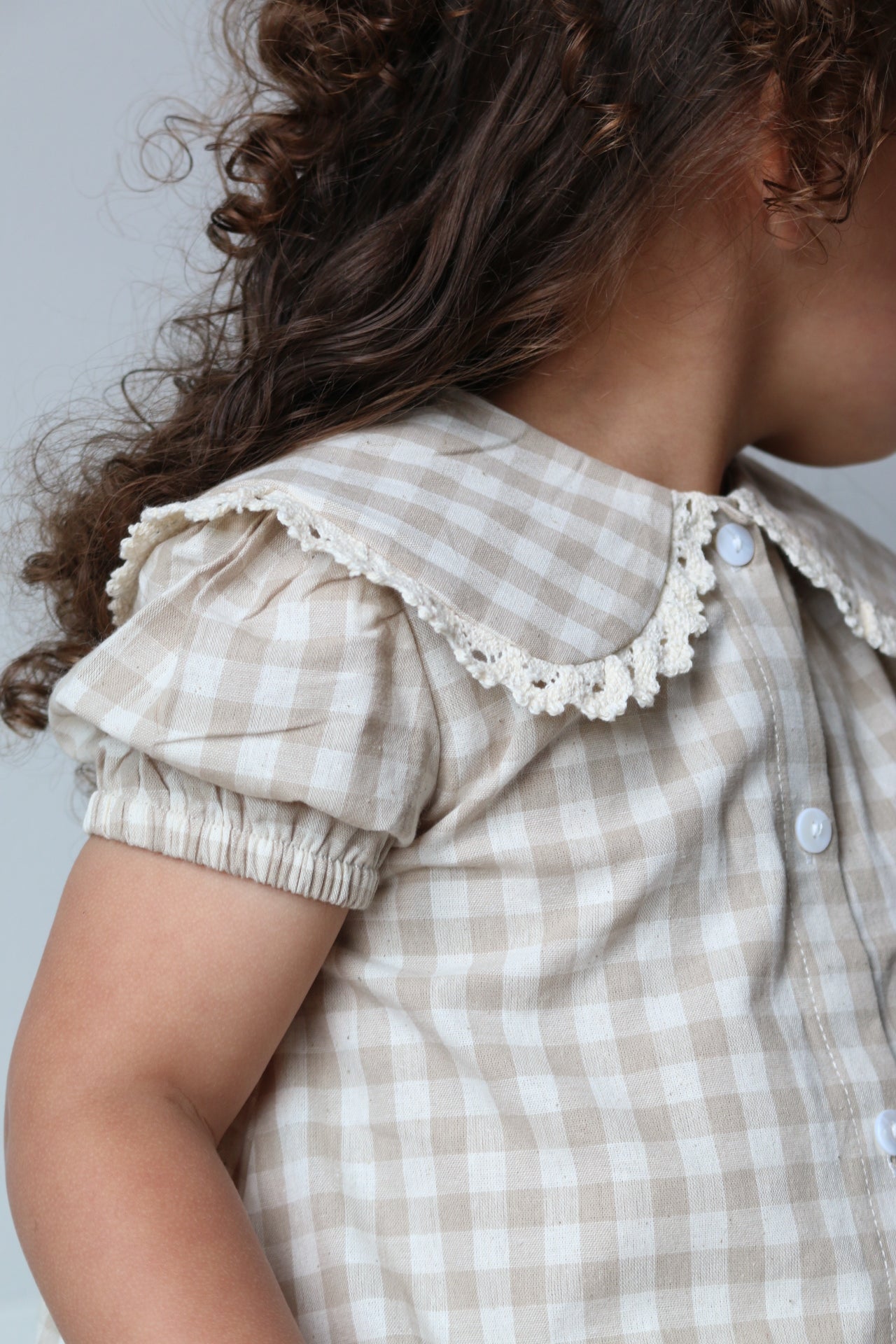 Person wearing a checkered dress with lace details on a light background