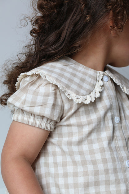 Person wearing a checkered dress with lace details on a light background