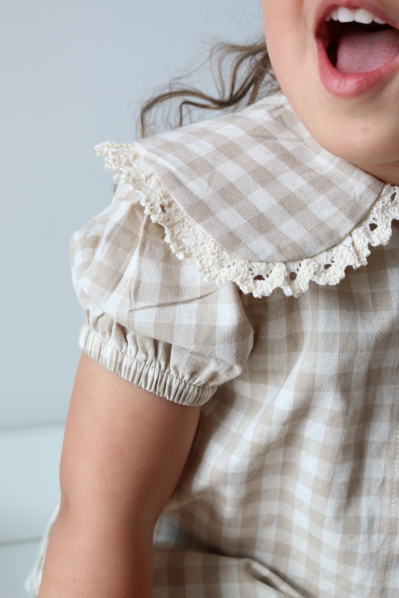 Close-up of a person wearing a checkered outfit with ruffled details on a light blue background