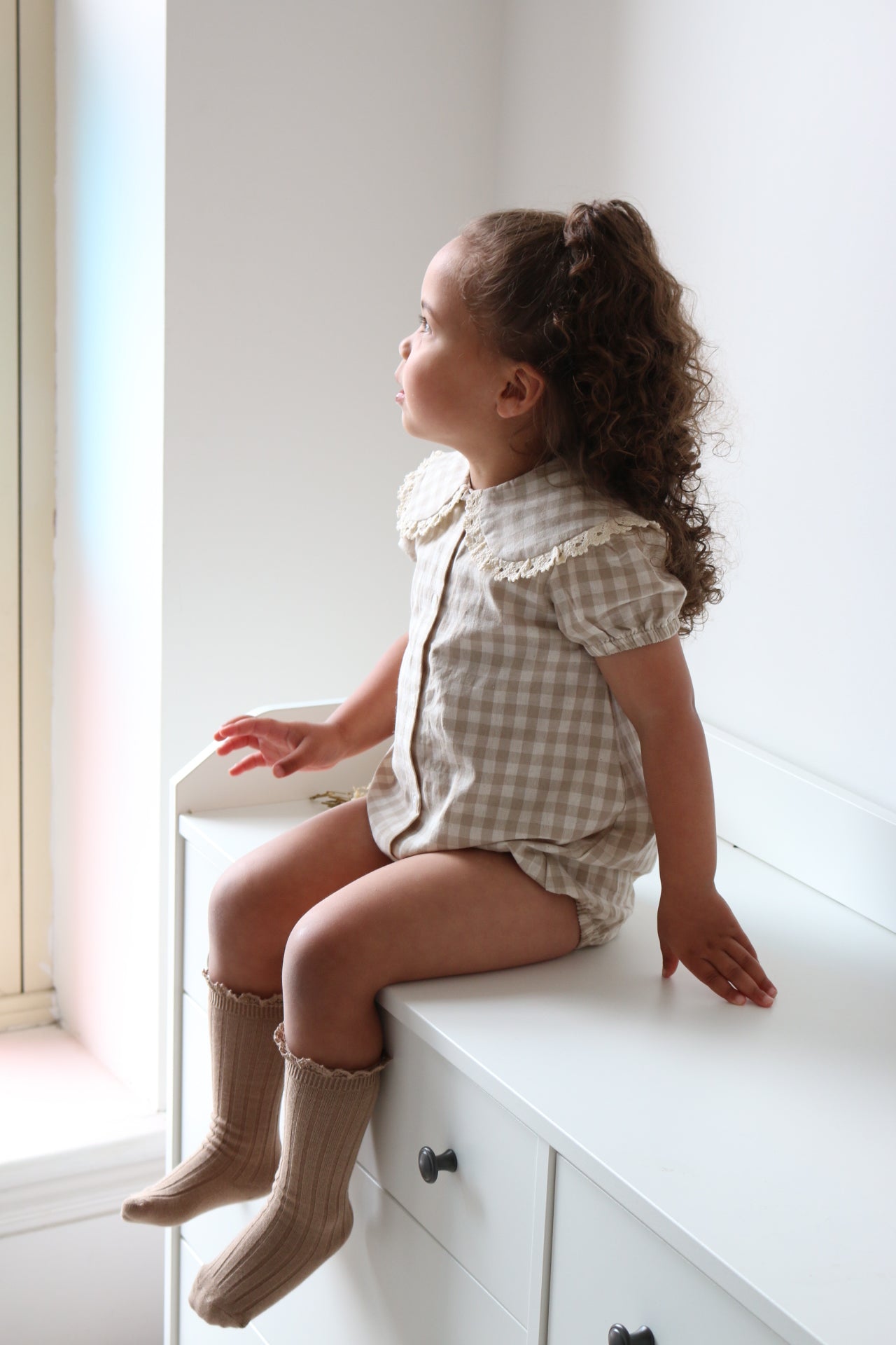 Child sitting on a white cabinet with a neutral background