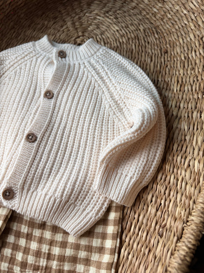 Ivory knitted cardigan, with the wooden buttons. Flat laid on a wicker basket. 