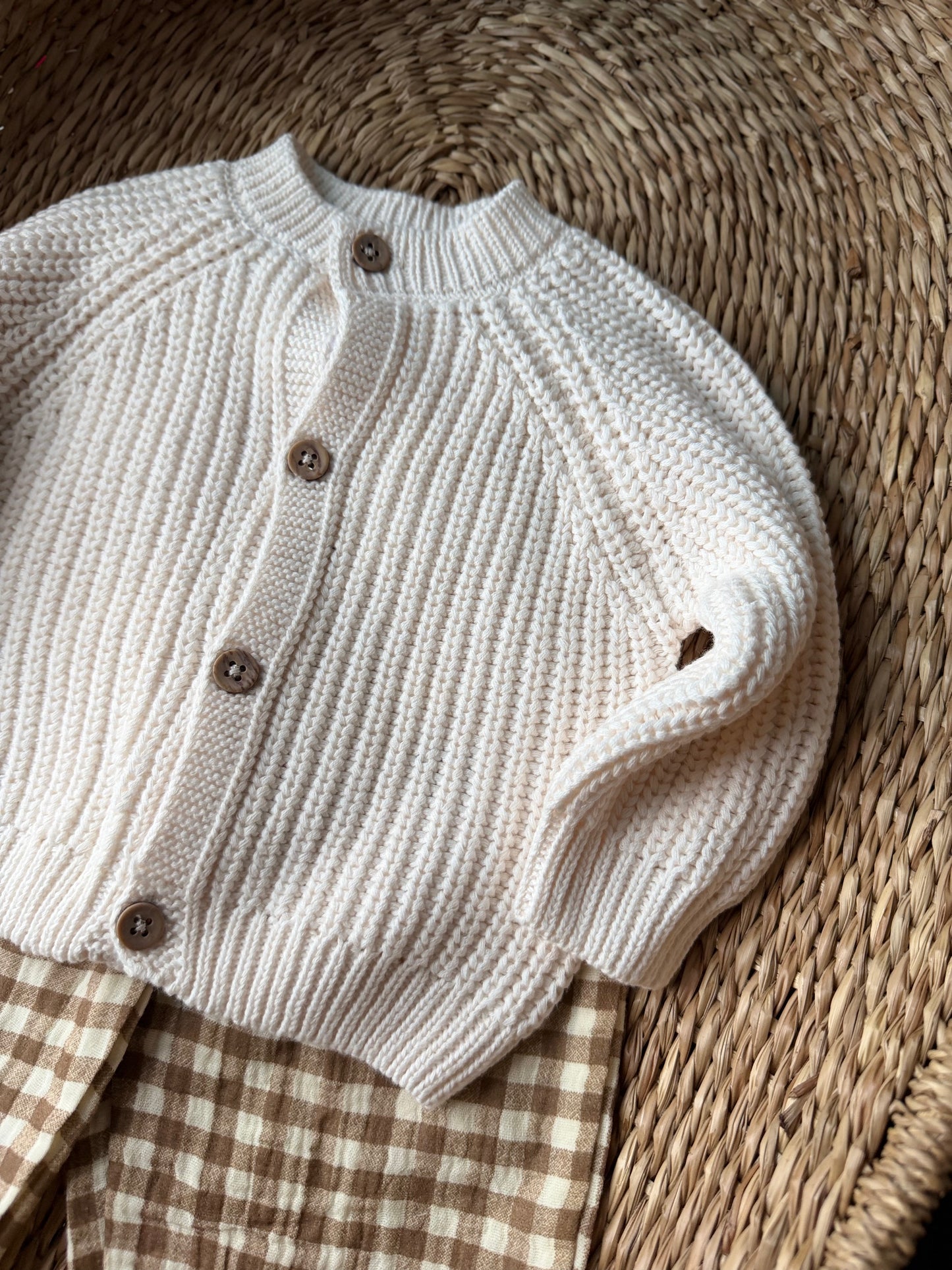 Knitted baby cardigan with wooden button flat laid on wicker basket. 