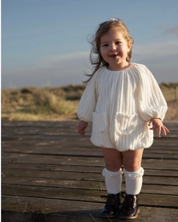 Child in a white outfit standing on a wooden boardwalk with a natural background