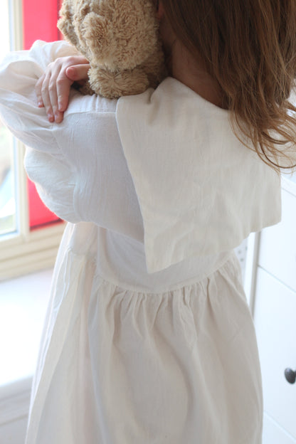 girl wearing a white dress holding a teddy bear indoors.