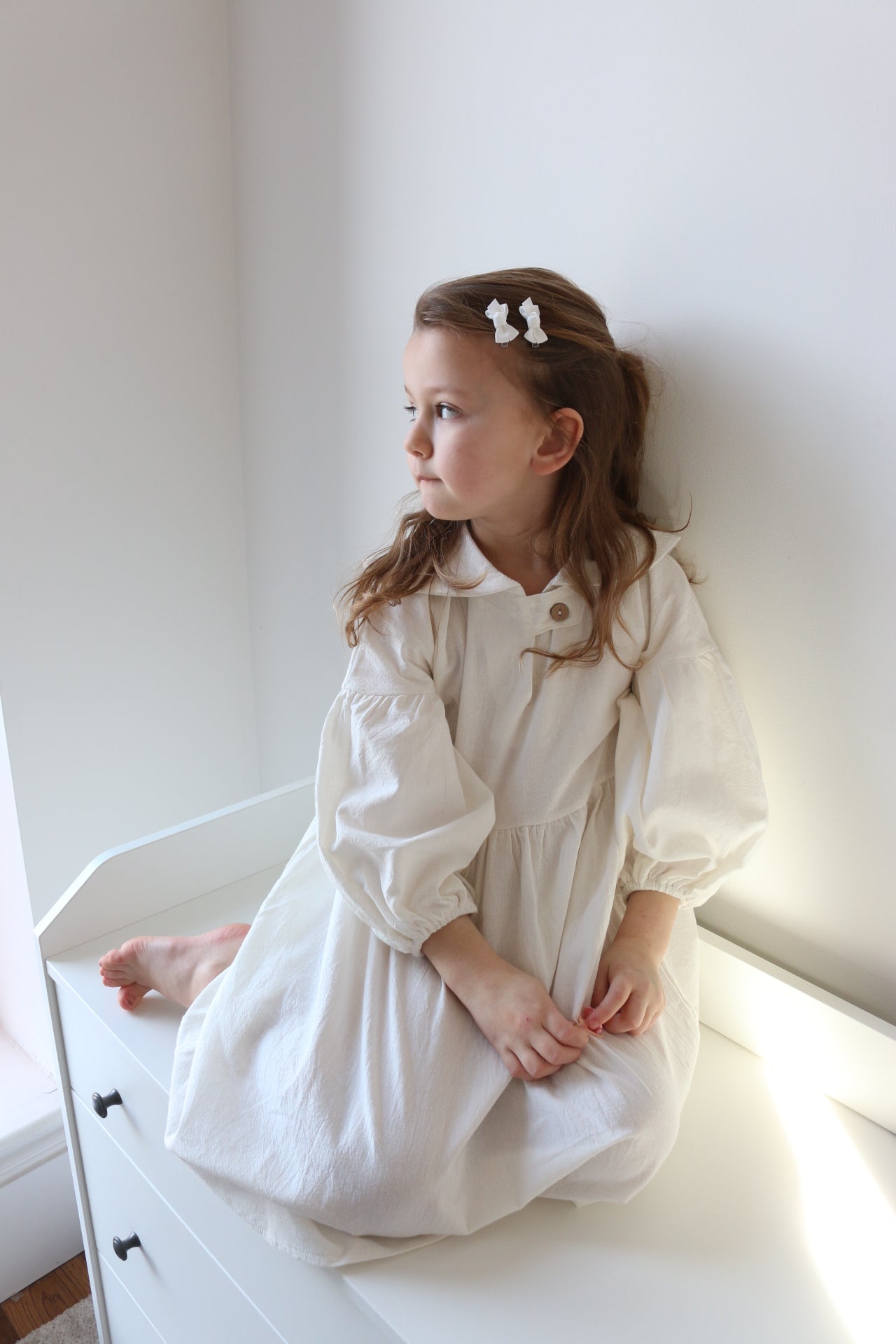 Young girl in a white dress lying on a white surface with a white wall in the background