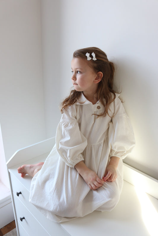 Young girl in a white dress lying on a white surface with a white wall in the background