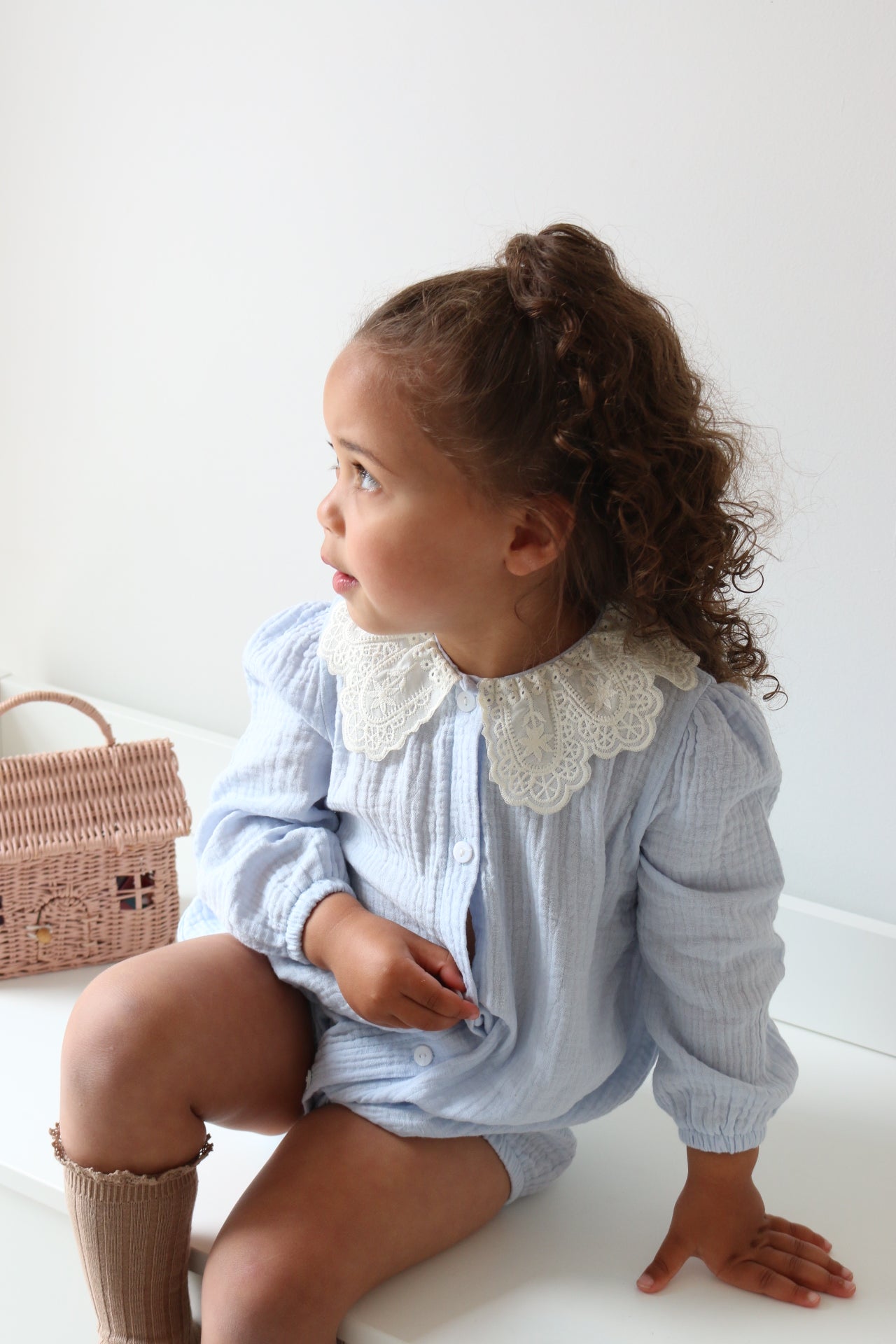 Child wearing a light blue outfit with a lace collar sitting on a white drawers