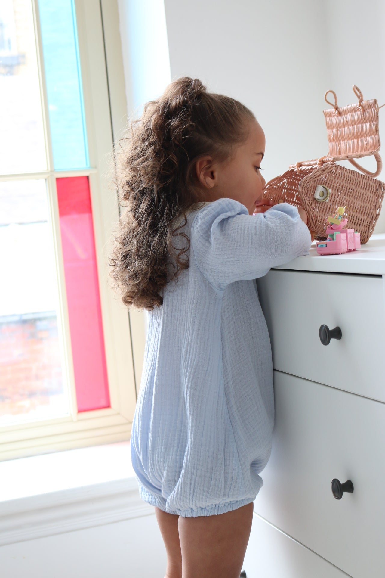Little girl standing against drawers playing in blue romper