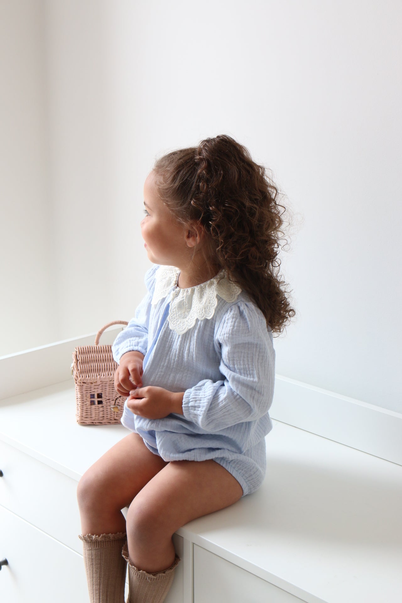 Child in a light blue romper standing on a white drawers