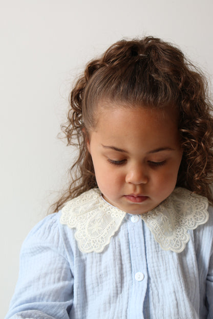 Child with curly hair wearing a light blue romper with lace details on a white background