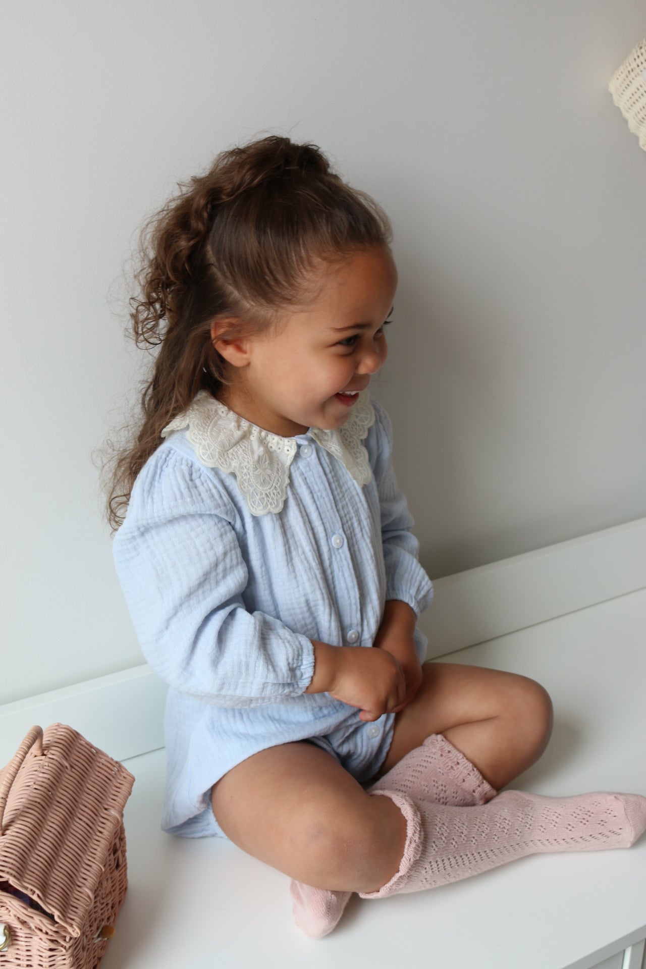 Child lying on a white drawers wearing a blue romper and pink socks.