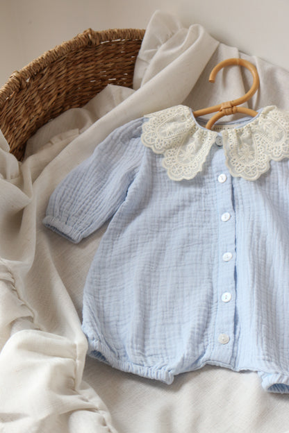 Light blue baby romper with lace details on a neutral background