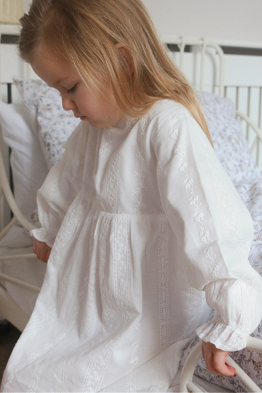  little girl, leaning on a bed wearing white cotton dress. 