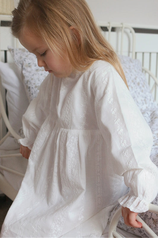  little girl, leaning on a bed wearing white cotton dress. 
