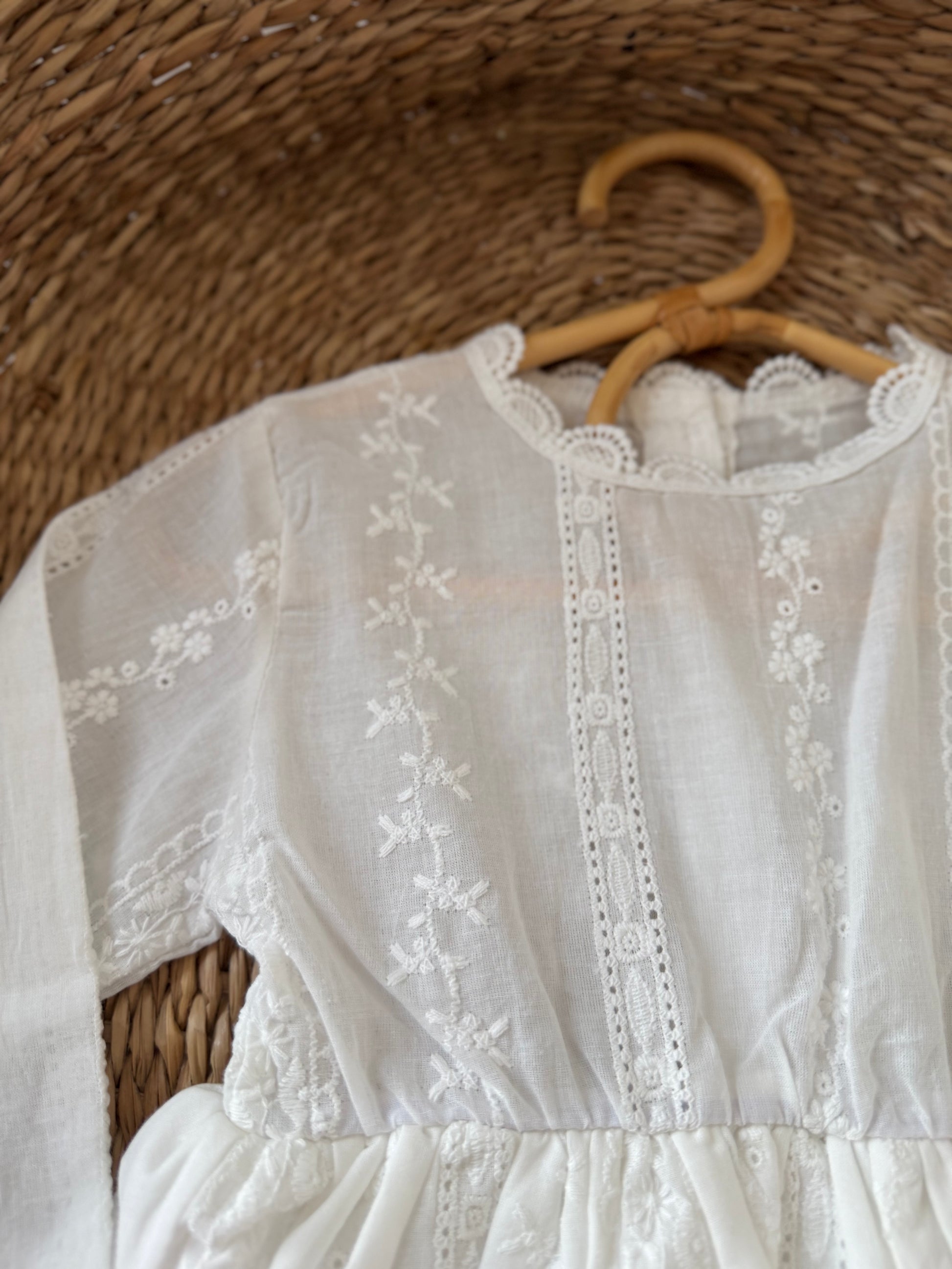White embroidered dress on a wooden hanger against a woven background