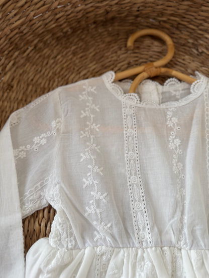 White embroidered dress on a wooden hanger against a woven background