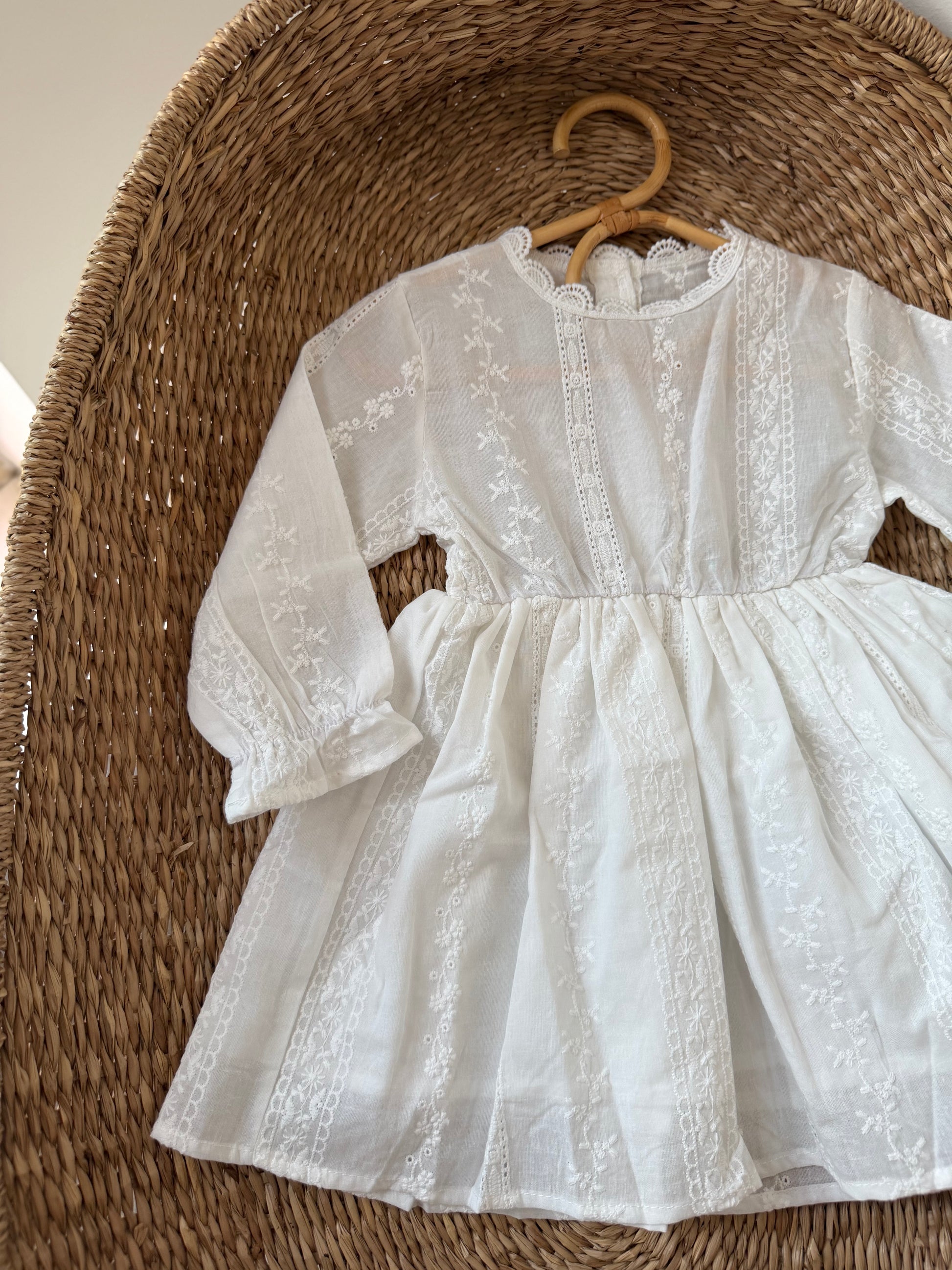 White cotton dress on a hanger against a woven basket background
