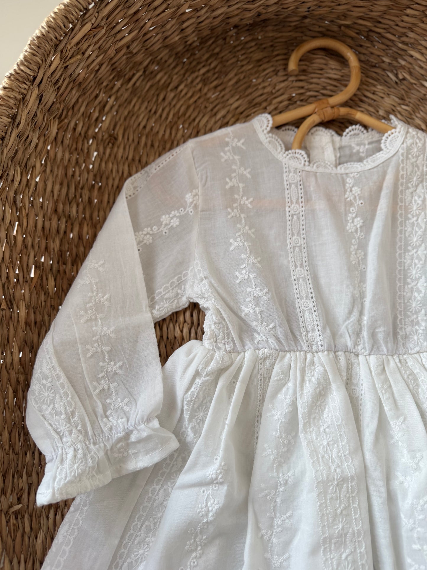 White lace dress on a wooden hanger against a woven basket background